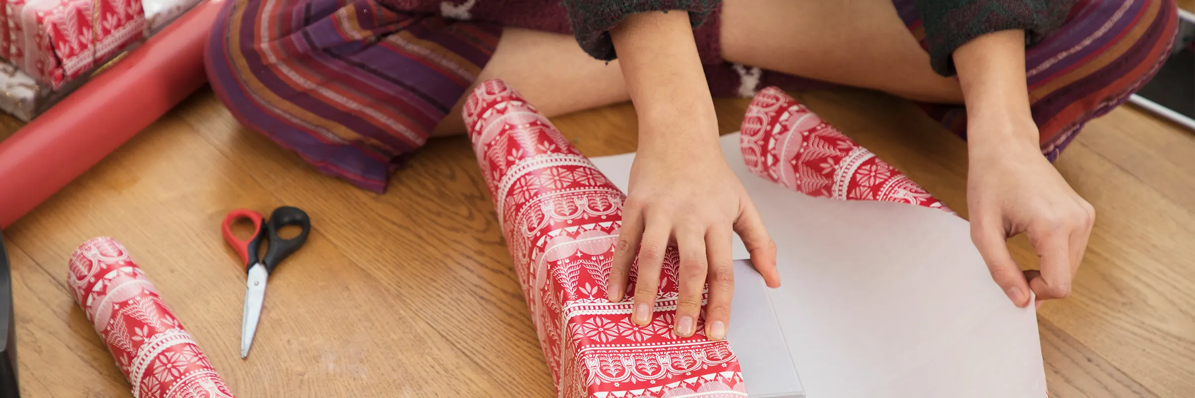 A person in pajamas wraps a holiday gift on the floor.