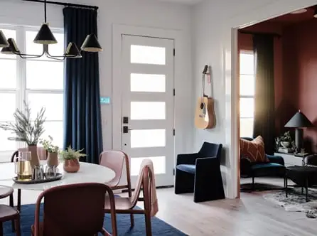 An entryway to a home is decorated with a seating area and a dining room table. Sunlight fills the room.