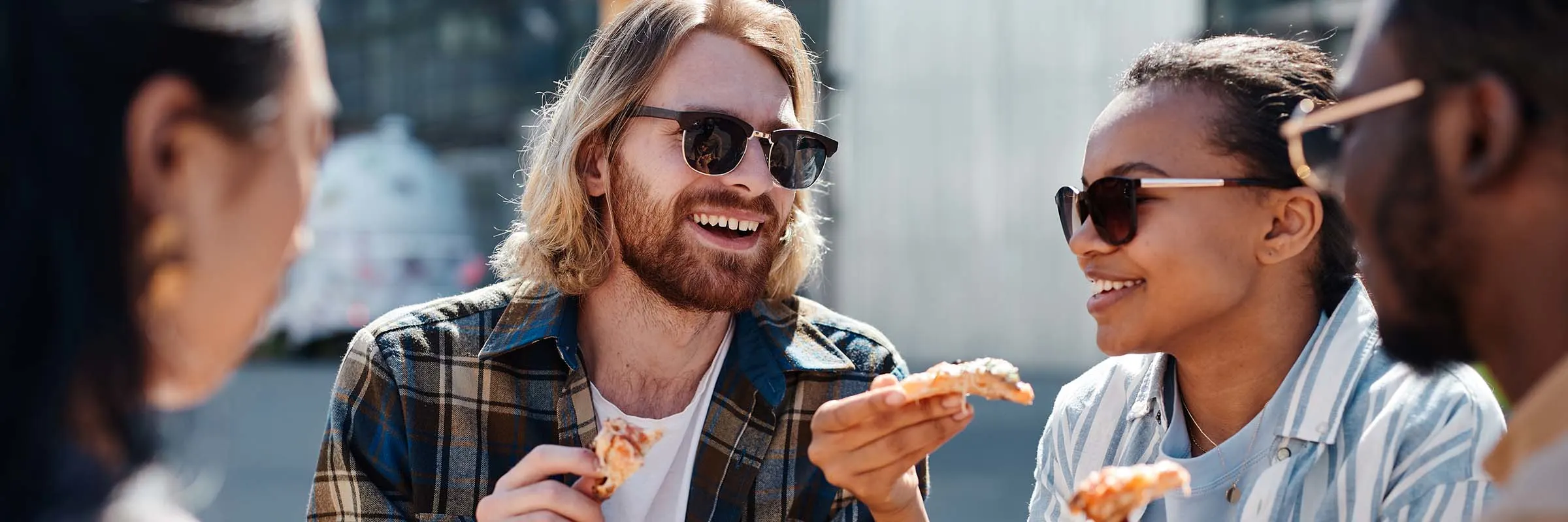 A group of friends is sitting outside and eating pizza. 