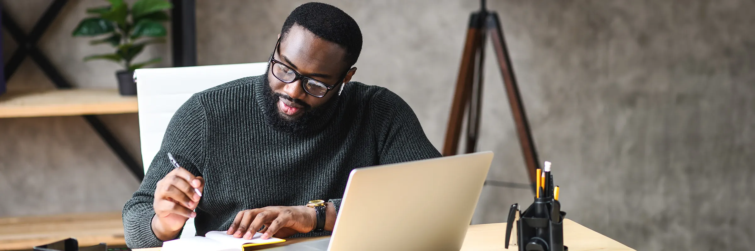 A man works at a desk with a laptop and notebook.

