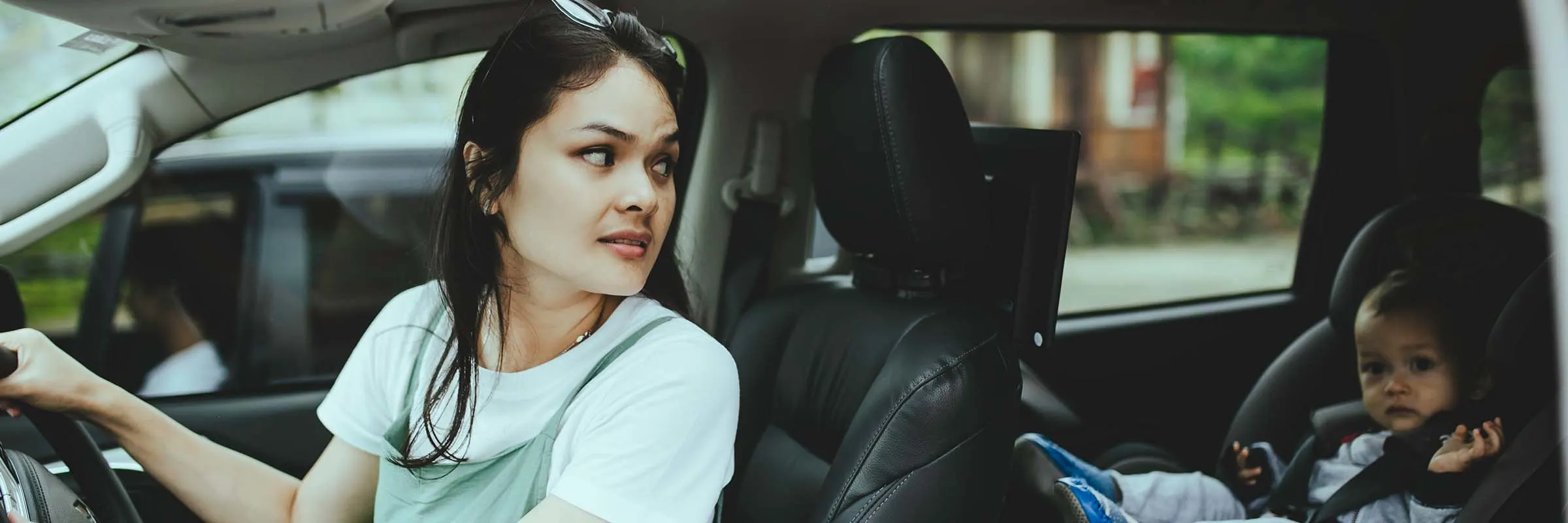 A woman in the driver's seat of a car looks back at her toddler in a car seat.