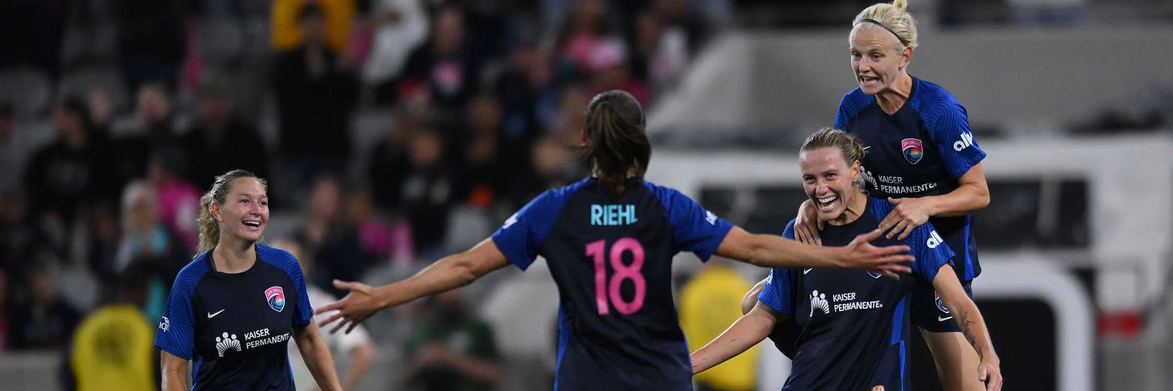  Four female soccer players run on the field in celebration