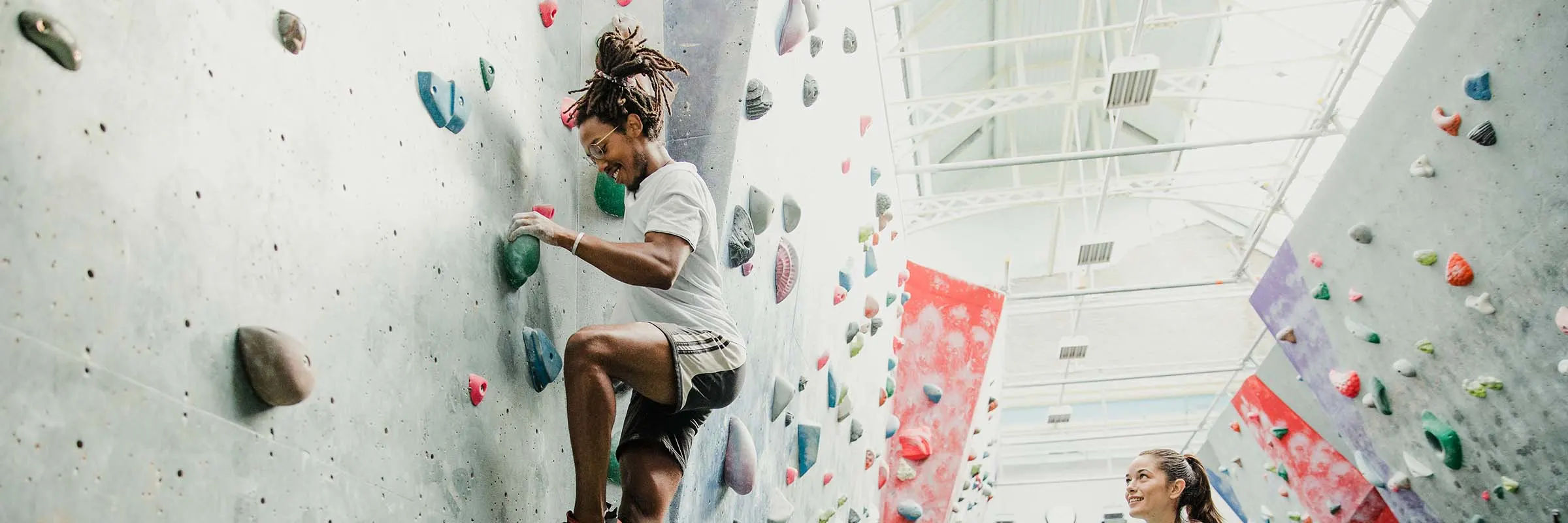 Beginner learns to rock climb on a bouldering wall with encouragement from a friend