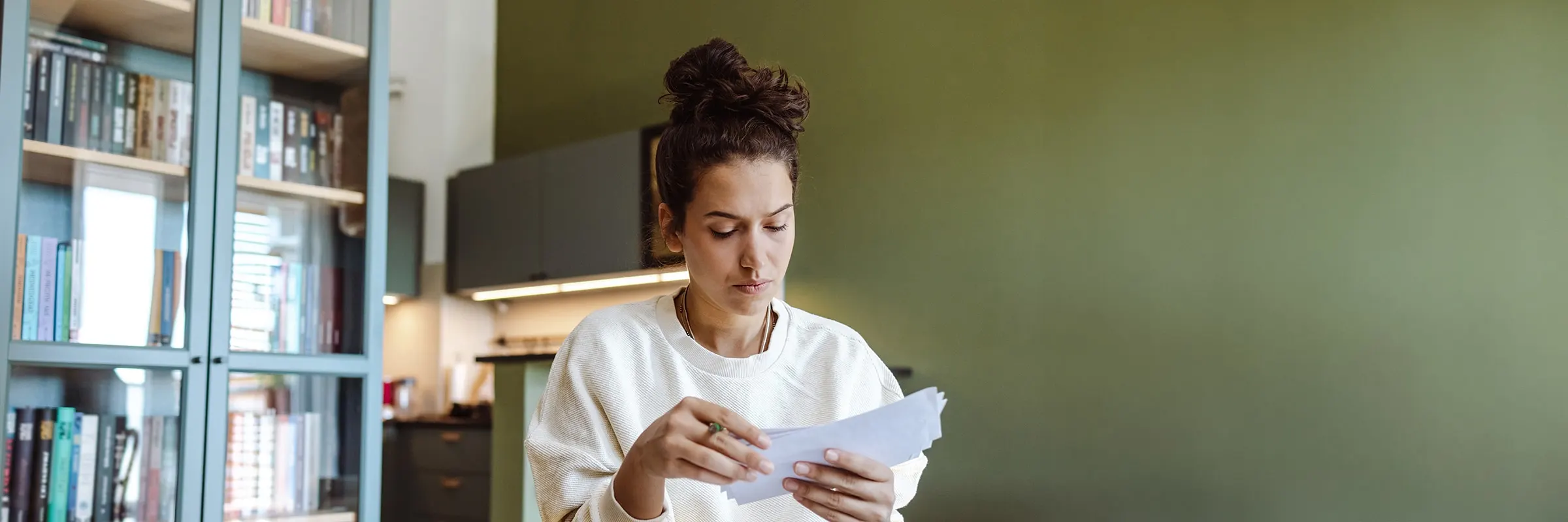 Young woman examines envelopes in her home office as she works on her budget.