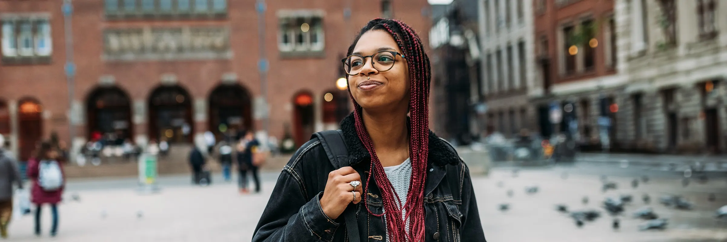 A woman wearing a backpack smiles as she pauses to enjoy a bustling city.