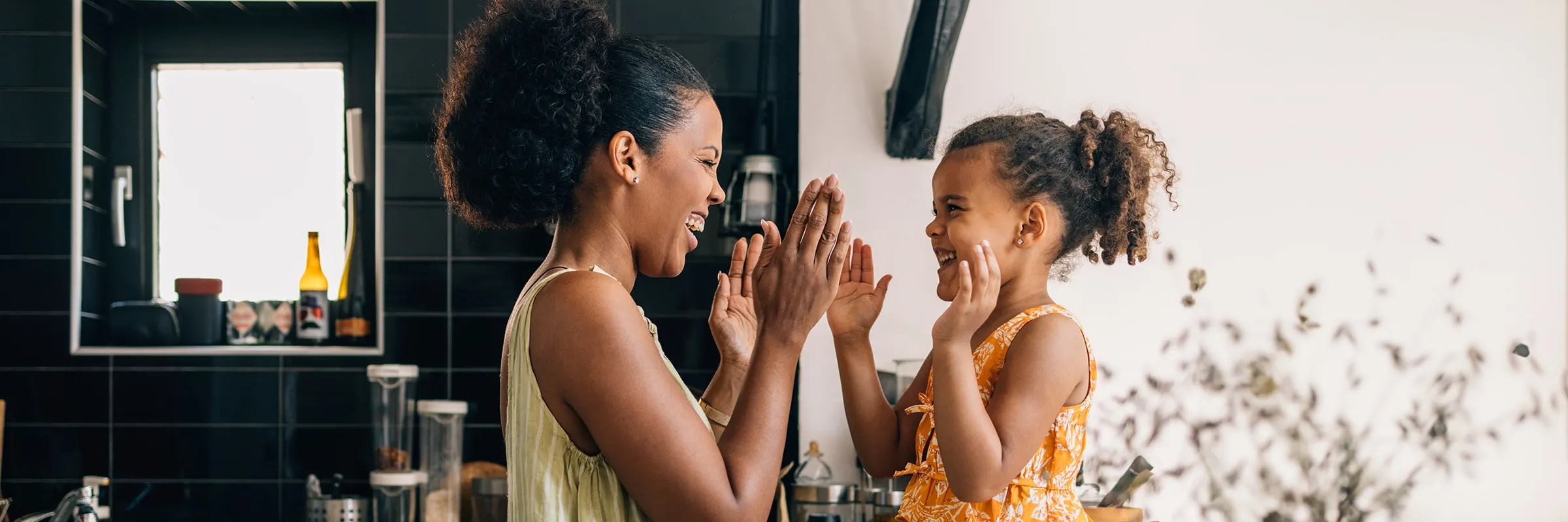 A mother and daughter smile while playing a game together in the kitchen of their home.