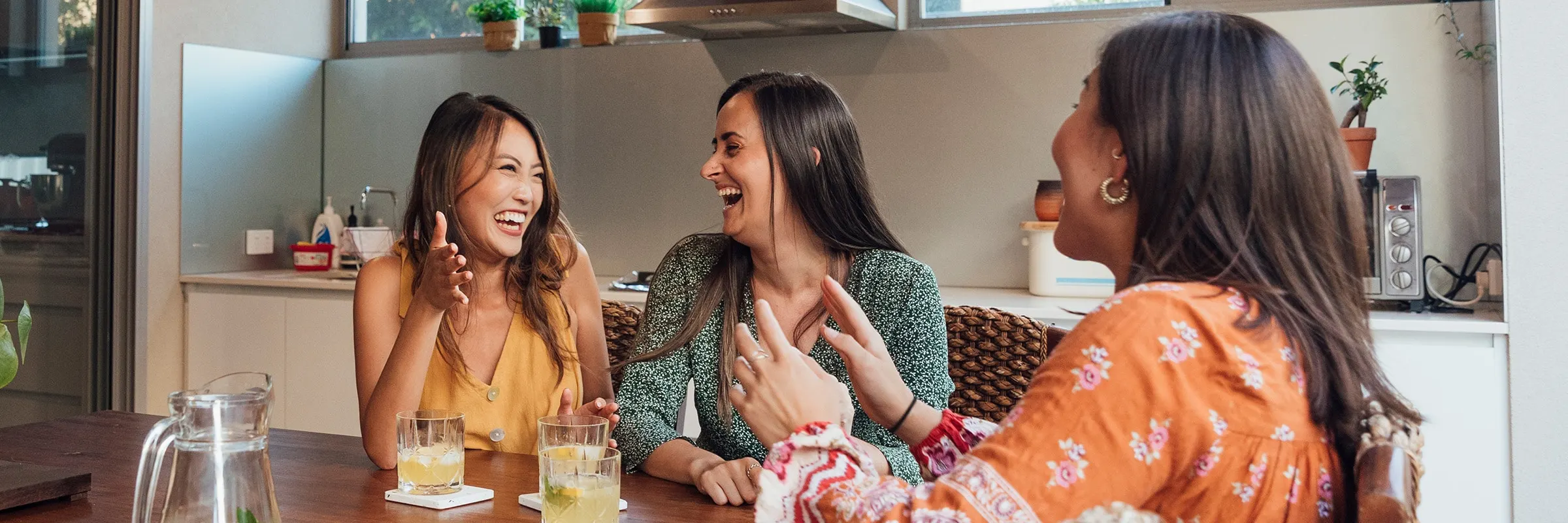 Three friends have a spirited chat while sitting around a large table.