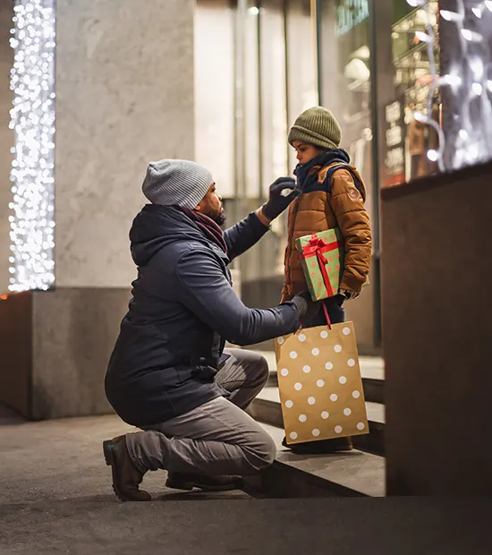Father kneeling in front of child to adjust his winter coat. 