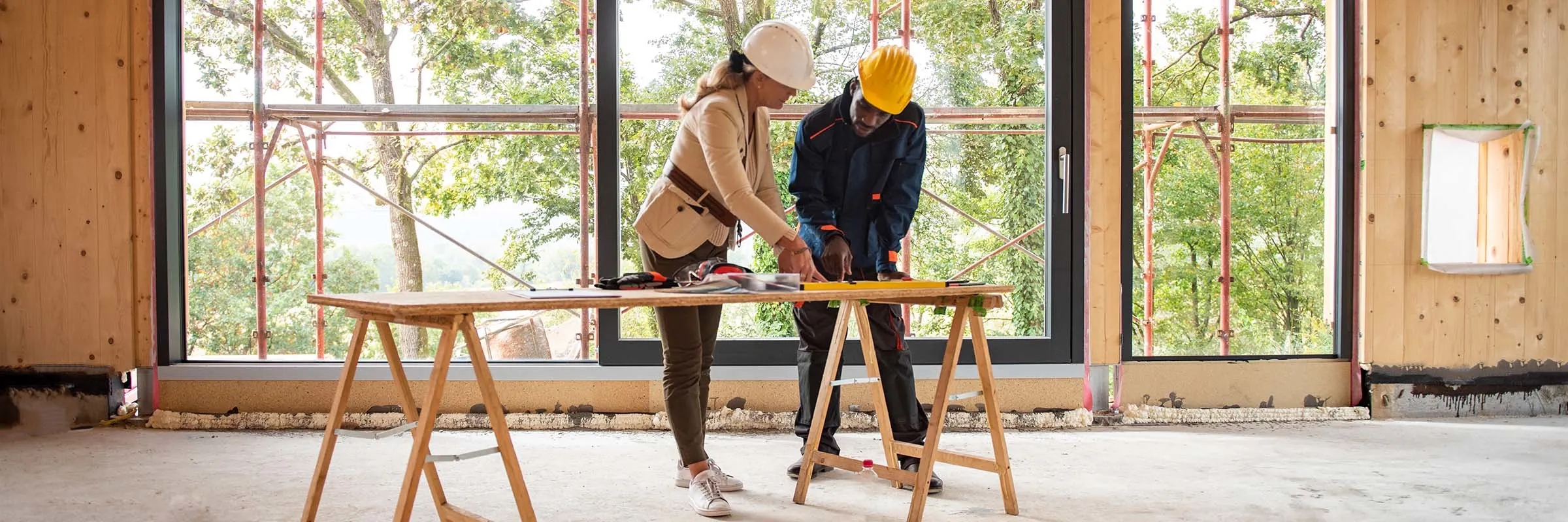 A man and woman stand inside a new construction and look at a blueprint for the home.