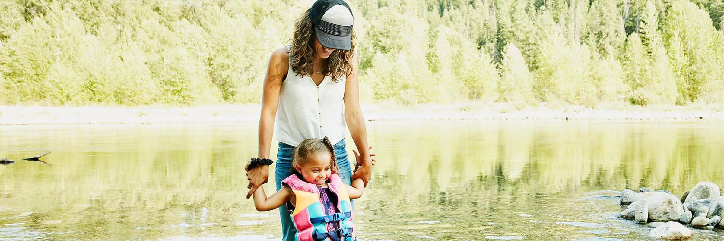 Smiling mother holding daughters hands while standing in river.