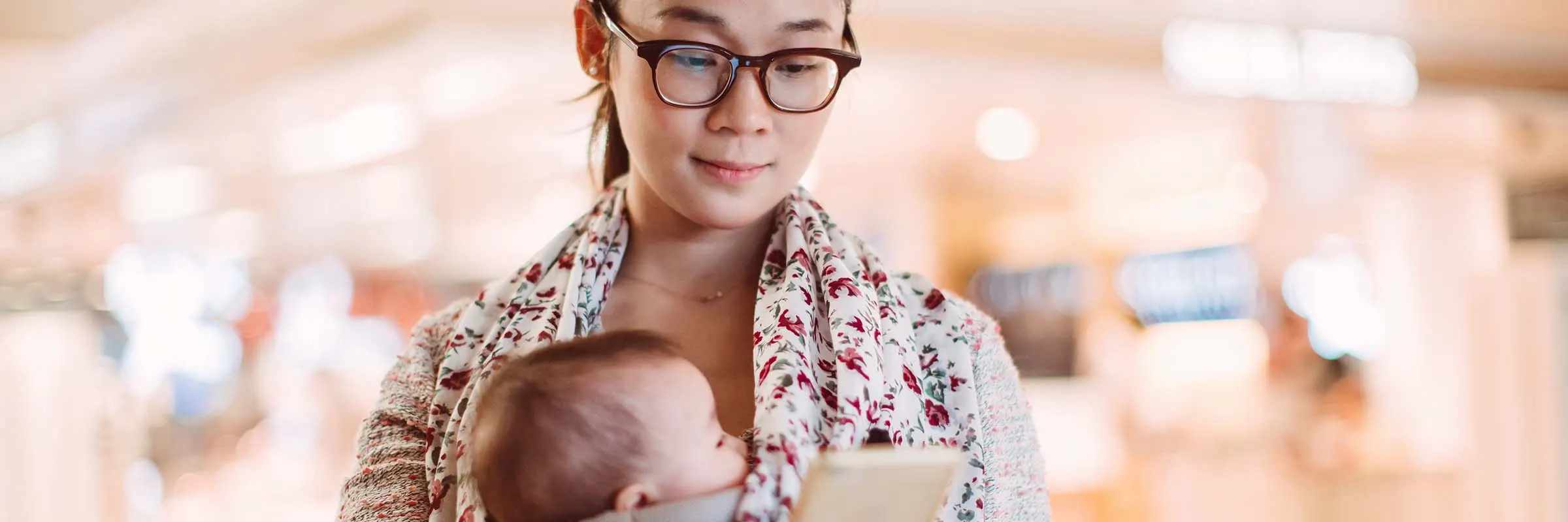 Young woman checks her phone while carrying a baby strapped in a front carrier