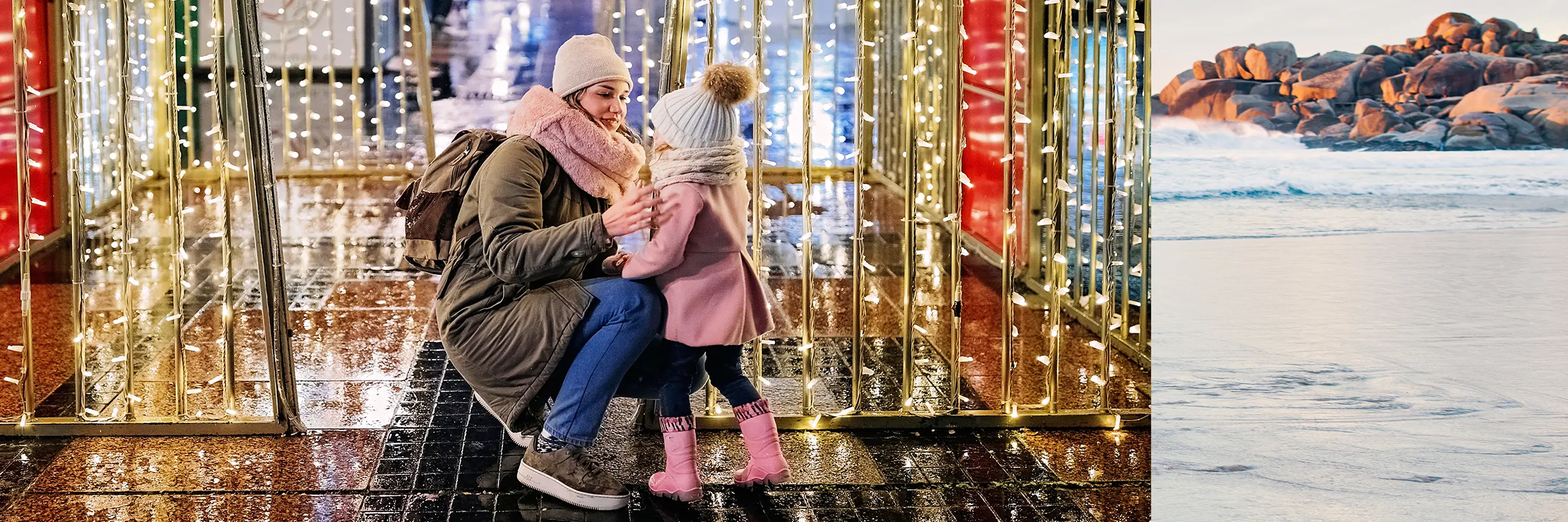 While standing in front of holiday lights outside, a mother kneels down to help her child with winter clothing 