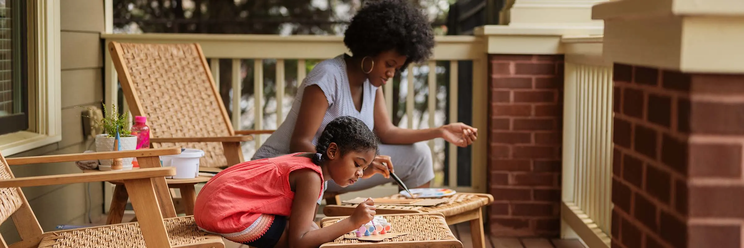 Mother and daughter paint while sitting in chairs on the front porch of their home.