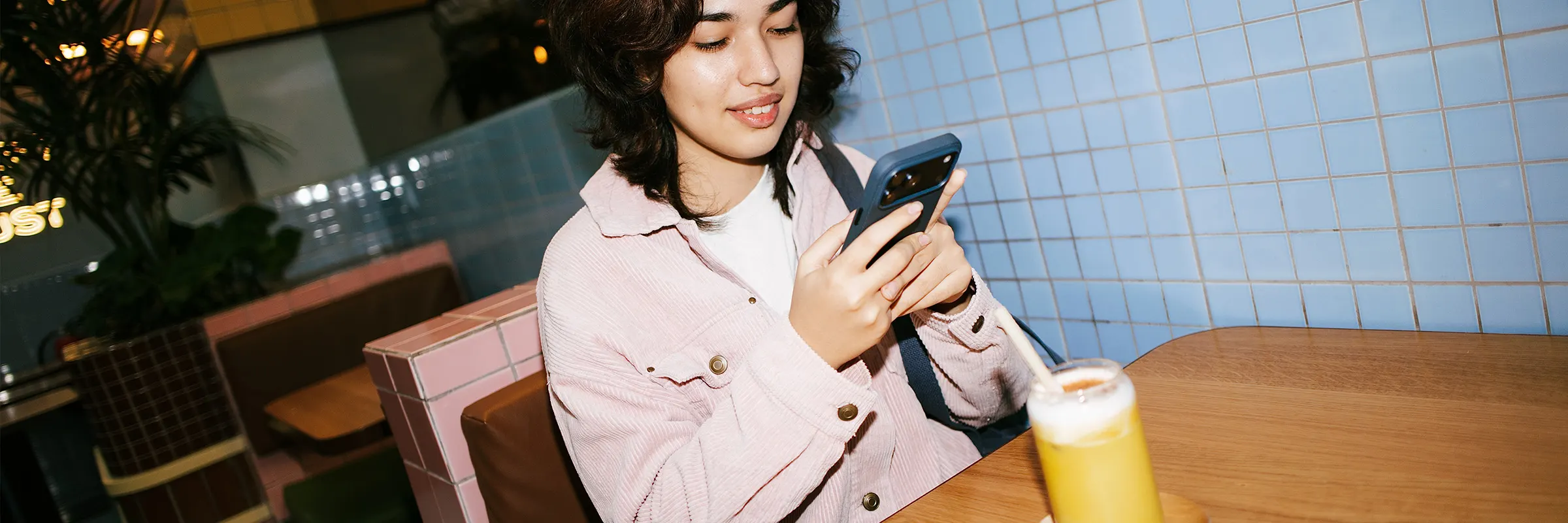 A young person sits at a cafe looking at their phone while enjoying a smoothie.
