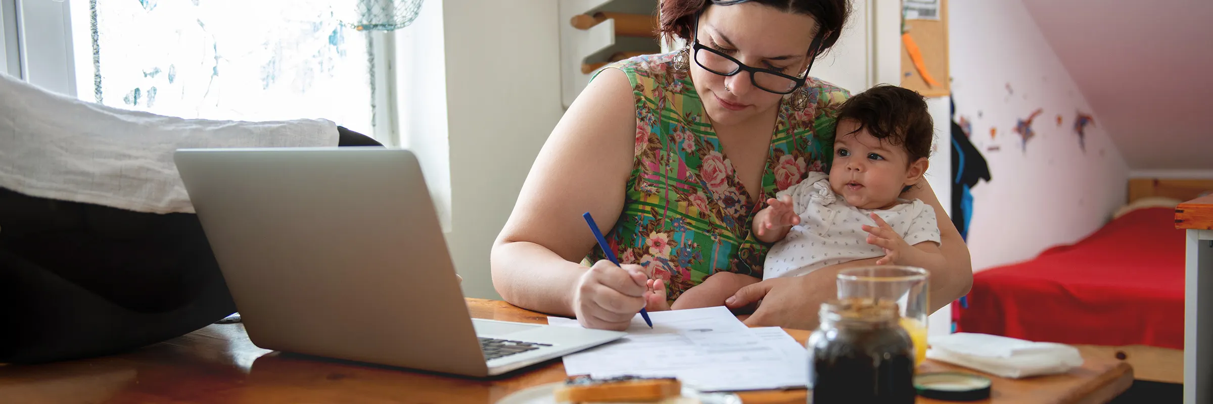 A woman works on paperwork while sitting at a table with her baby in her lap.