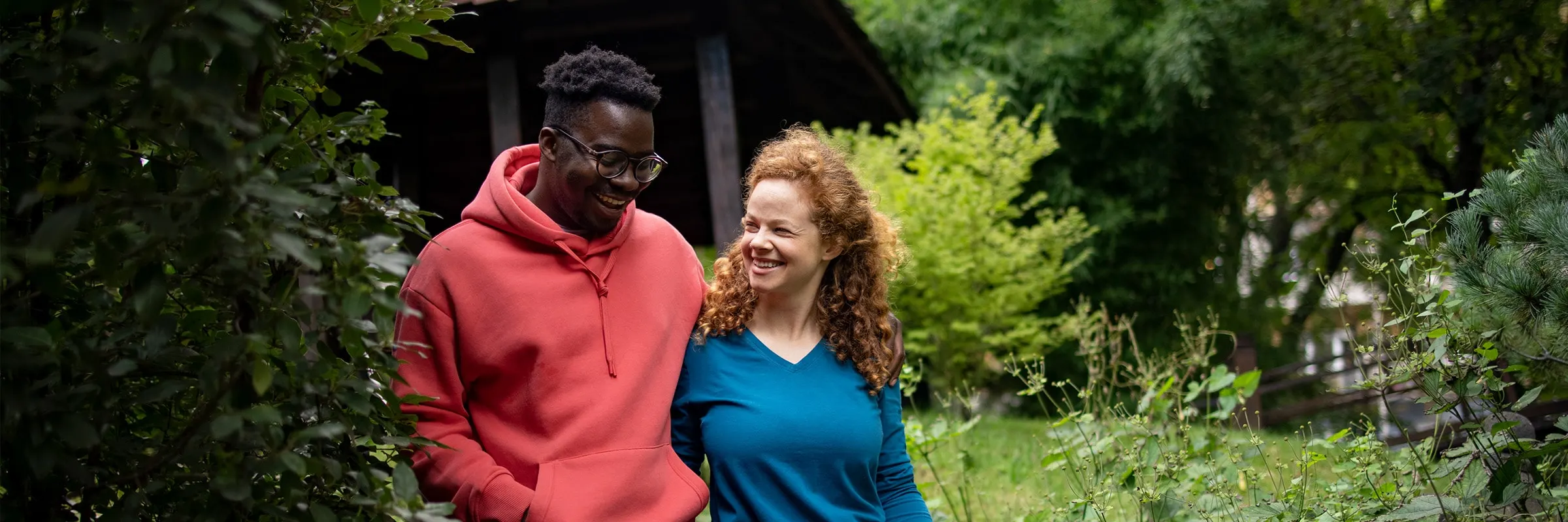 Happy couple walks through the wooded yard behind their house