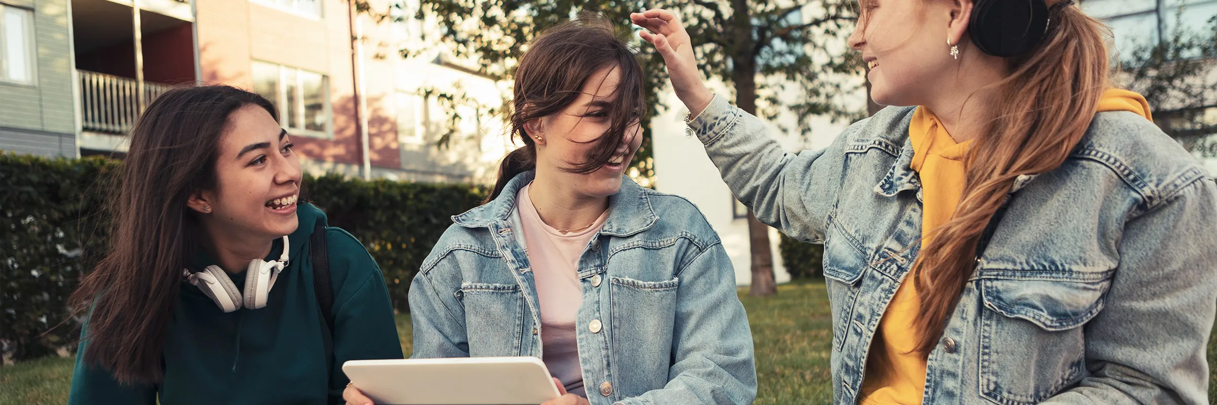 Three young women sitting outside their apartment, the woman in the middle is holding a tablet.