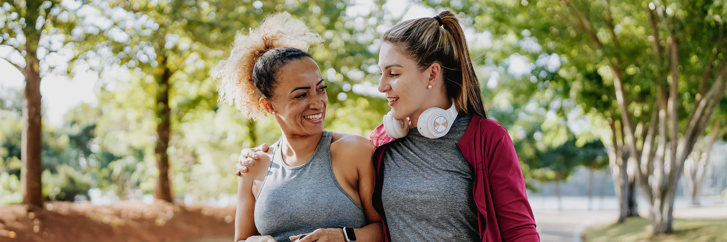 Two women in workout wear walk in the park.