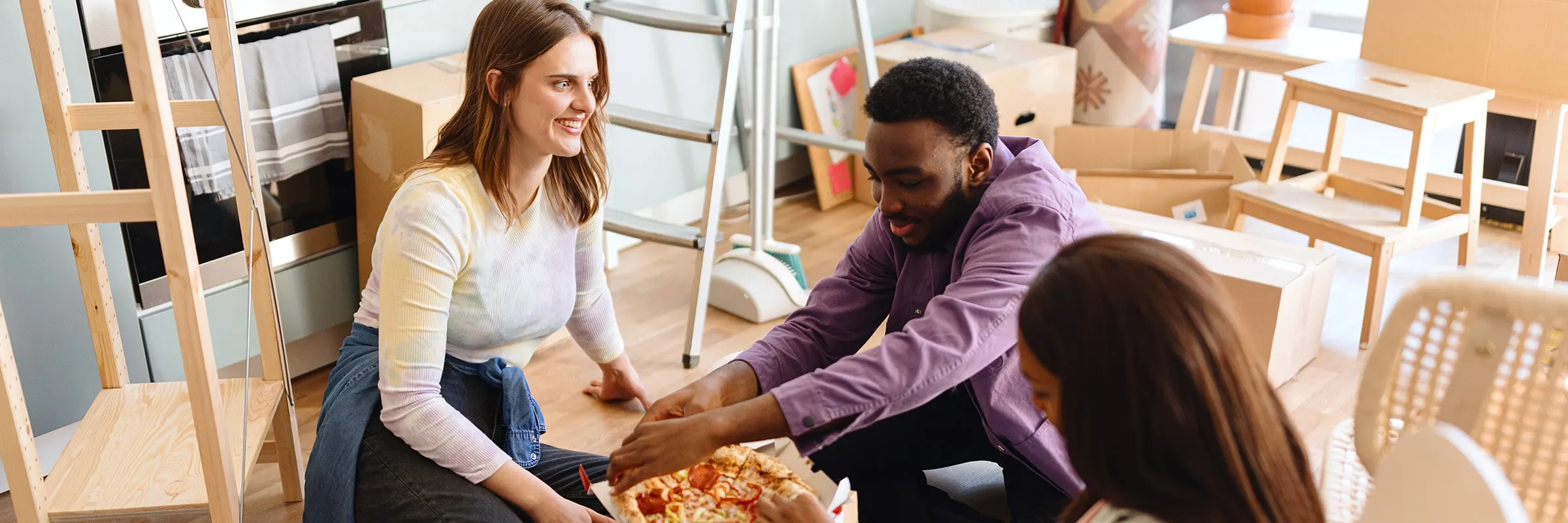 A group of friends takes a break from packing moving boxes to share a pizza.