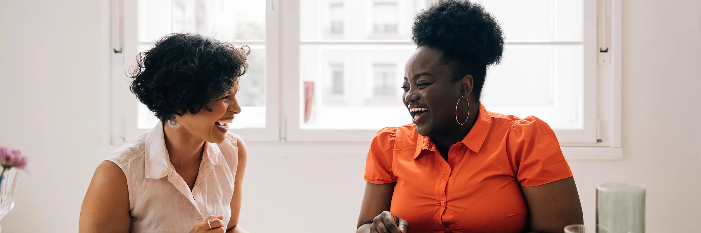 two people laugh together as they sit at a table full of food
