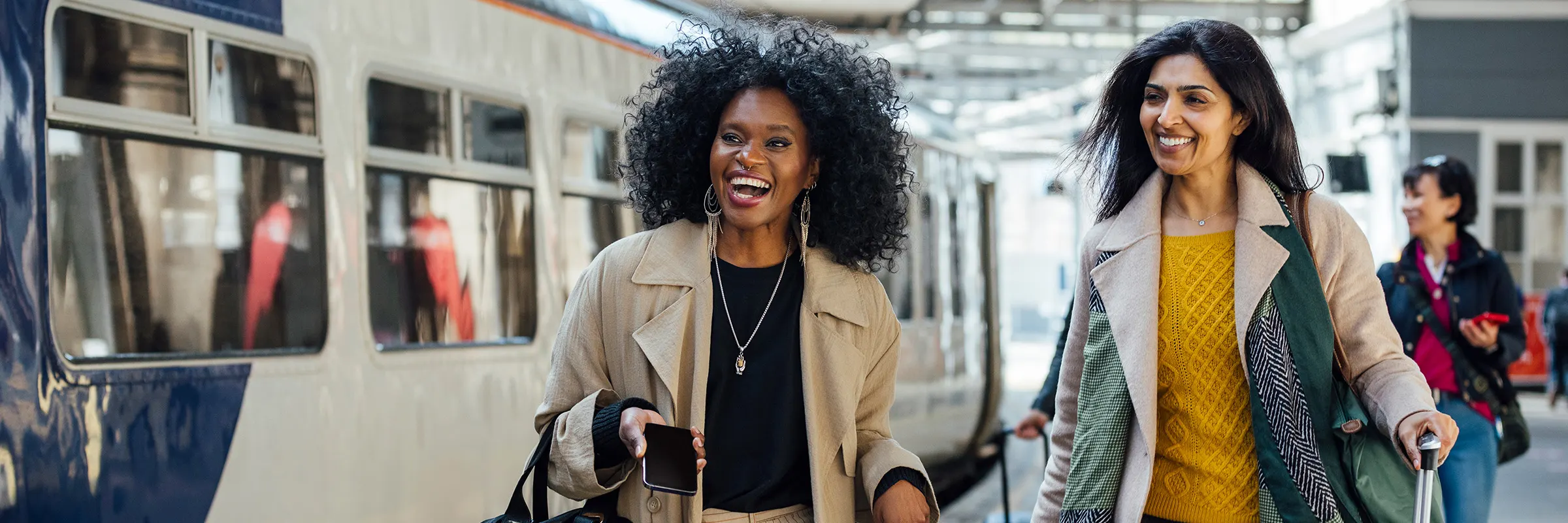 Two women smile as they walk down the platform in a train station.