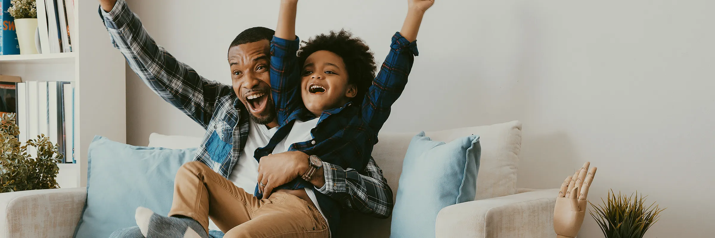 Son sits on his father's lap on the couch while they both smile. 