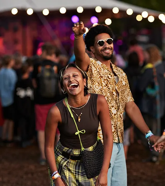 Two friends laughing together at an outdoor concert. 