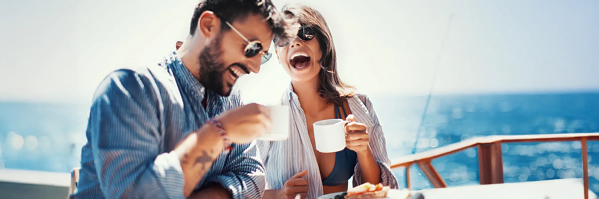 Young couple laughing and drinking coffee waterside