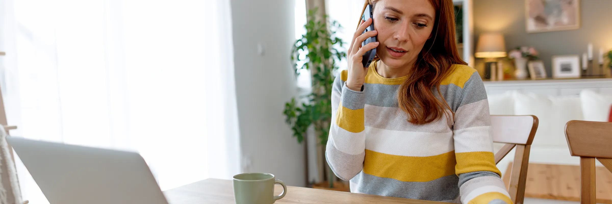 A person sitting at their kitchen table looking at documents while on the phone.