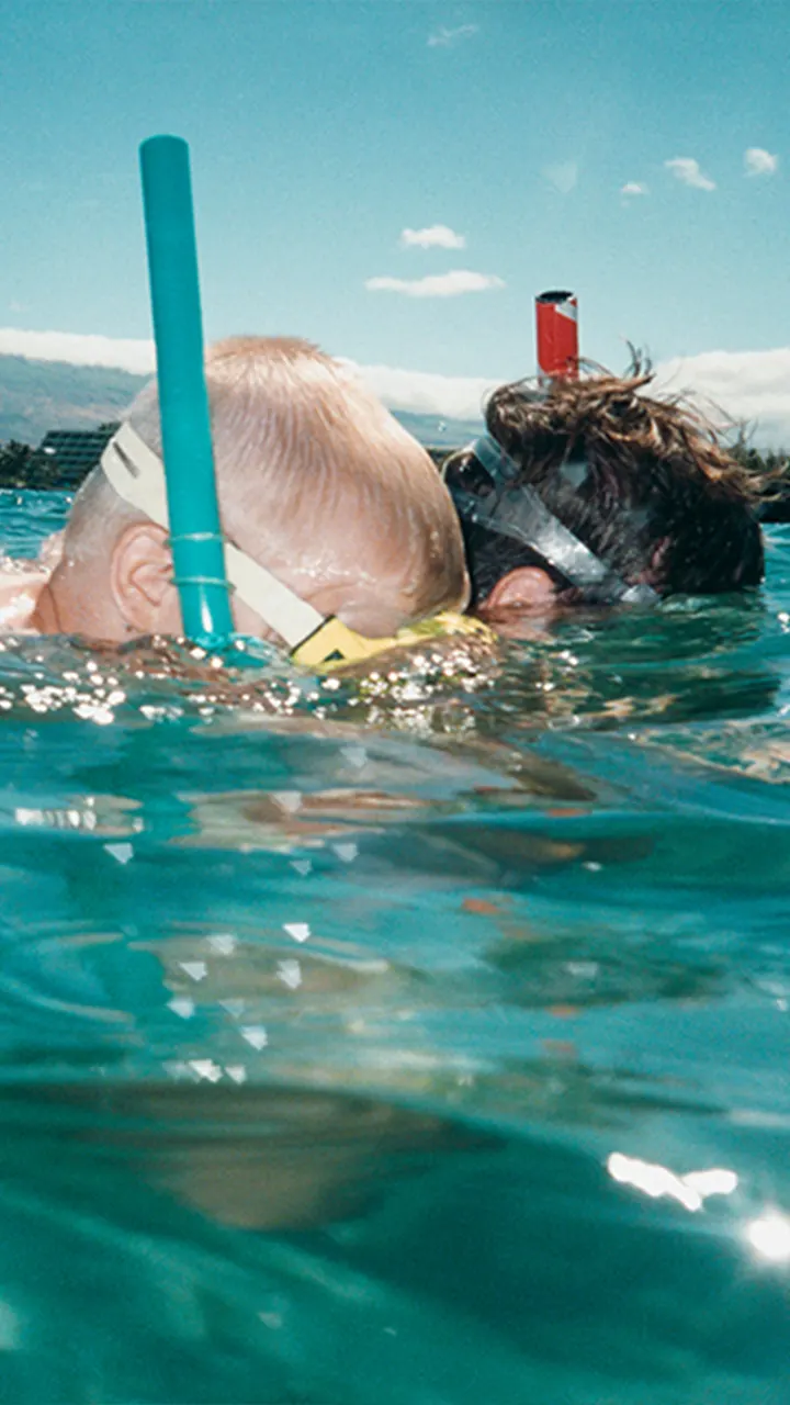 Parent and child snorkeling in the ocean. 