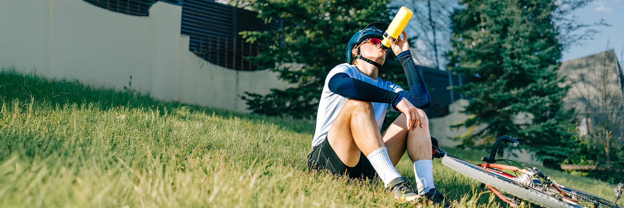 Cyclist drinking from a water bottle while resting on grassy hillside.