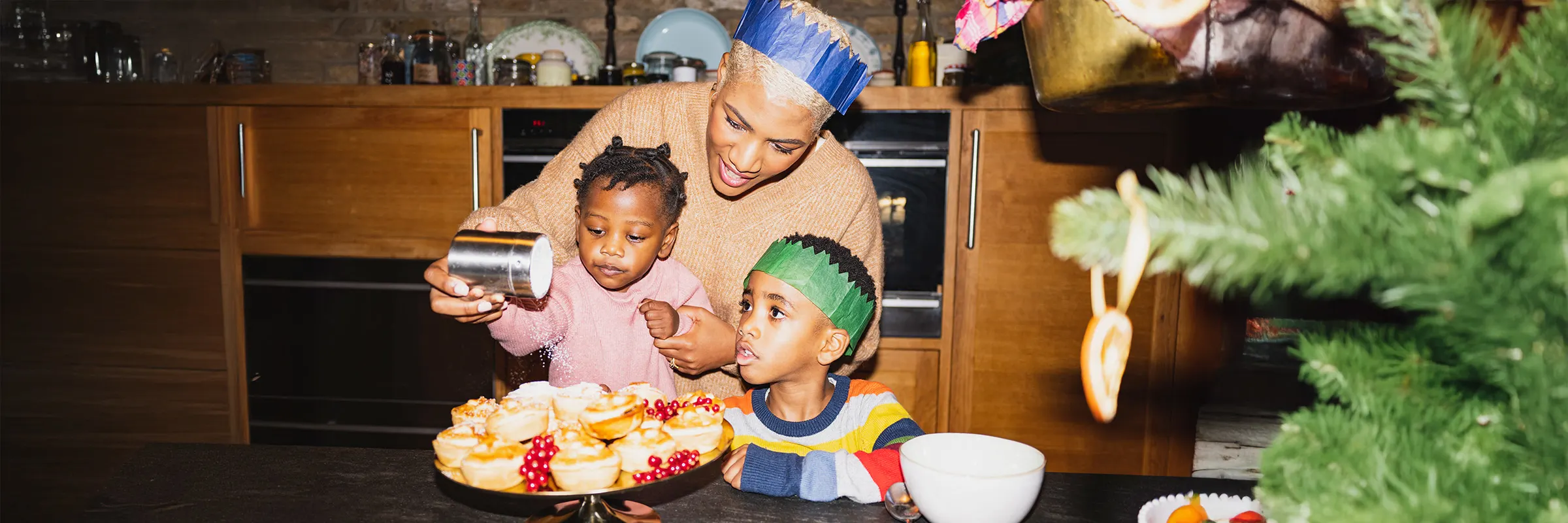 A parent stands behind two young children while they decorate food for a celebration