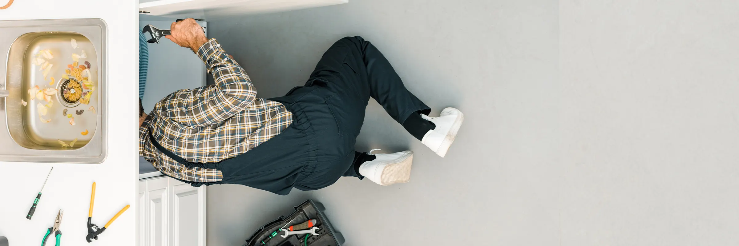 Birdseye view of a plumber’s legs hanging out from under a kitchen sink while they work. 