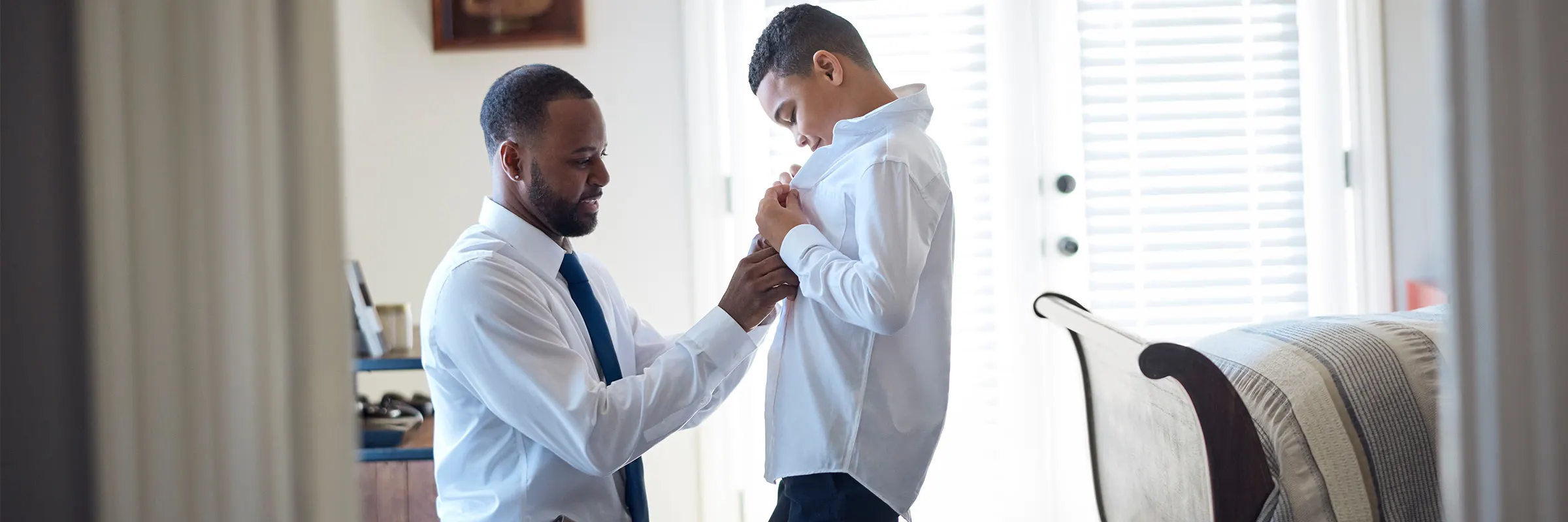 A father helps his son button up a dress shirt.