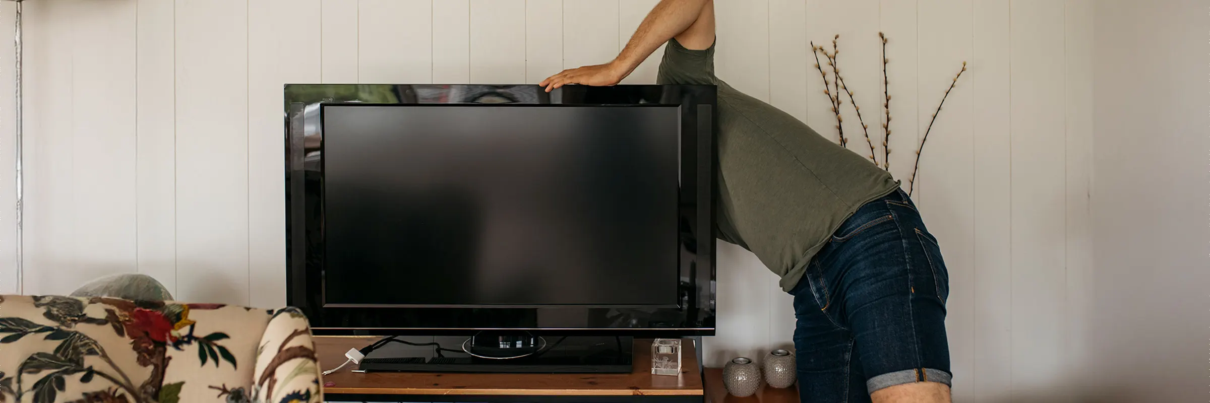 A person reaching behind a TV to install it.