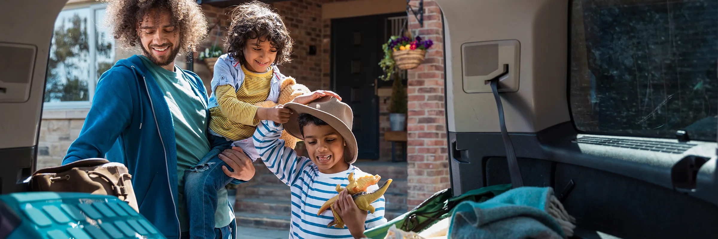 A father and his two young sons pack up the back of their car as they prepare for vacation.