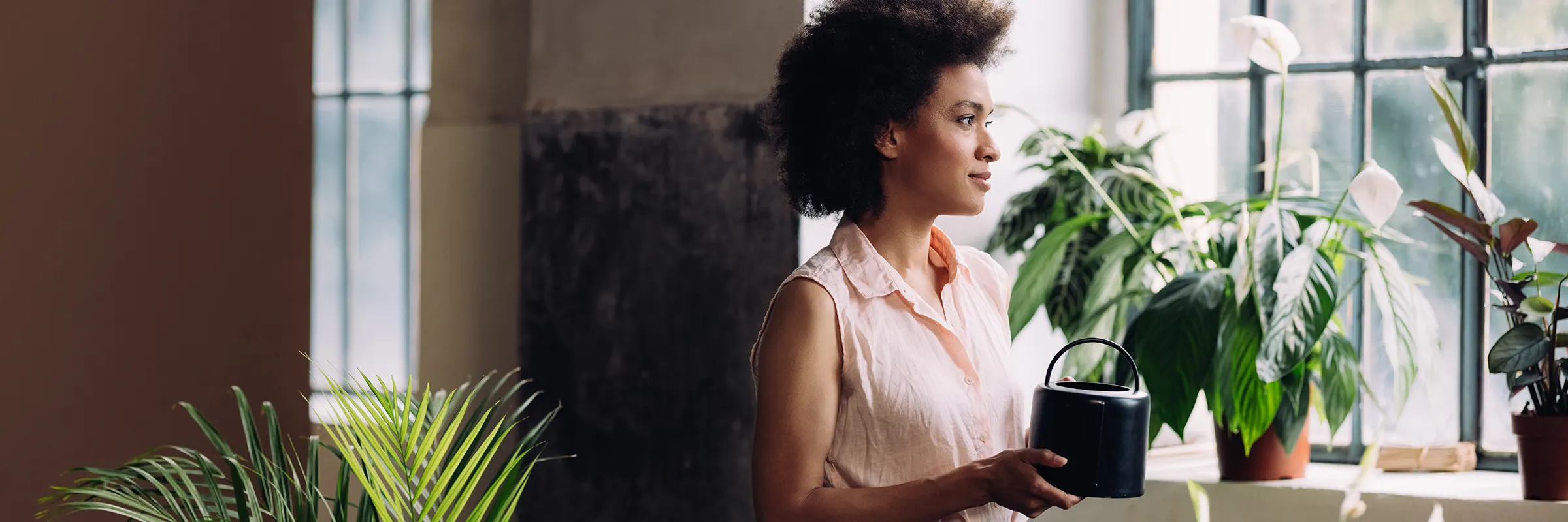 Woman watering her plants on a windowsill. 
