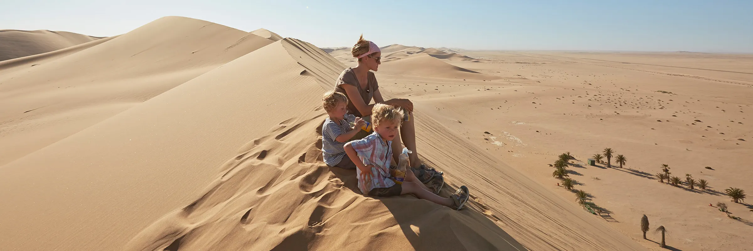 Mother and two children sit on top of a sand dune and look out over the landscape. 