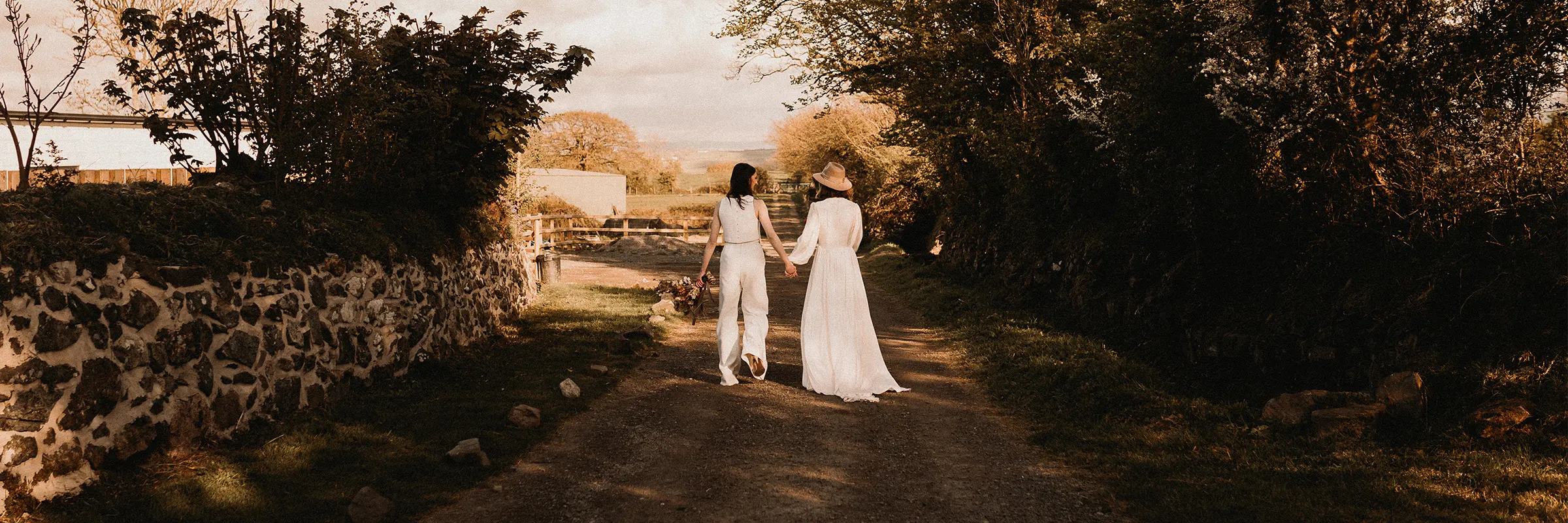 Young couple in wedding clothes walks down a dirt countryside road