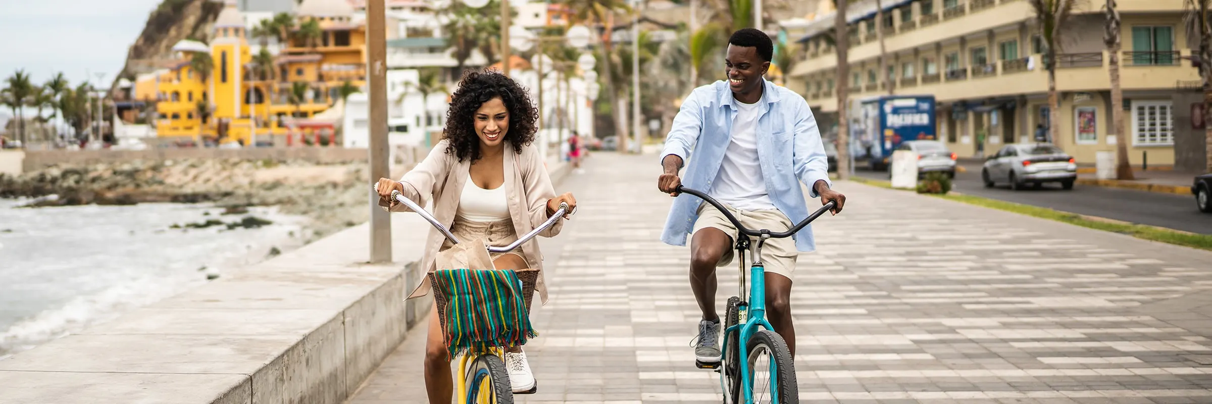 Young couple riding bikes down a beach boardwalk while on vacation.