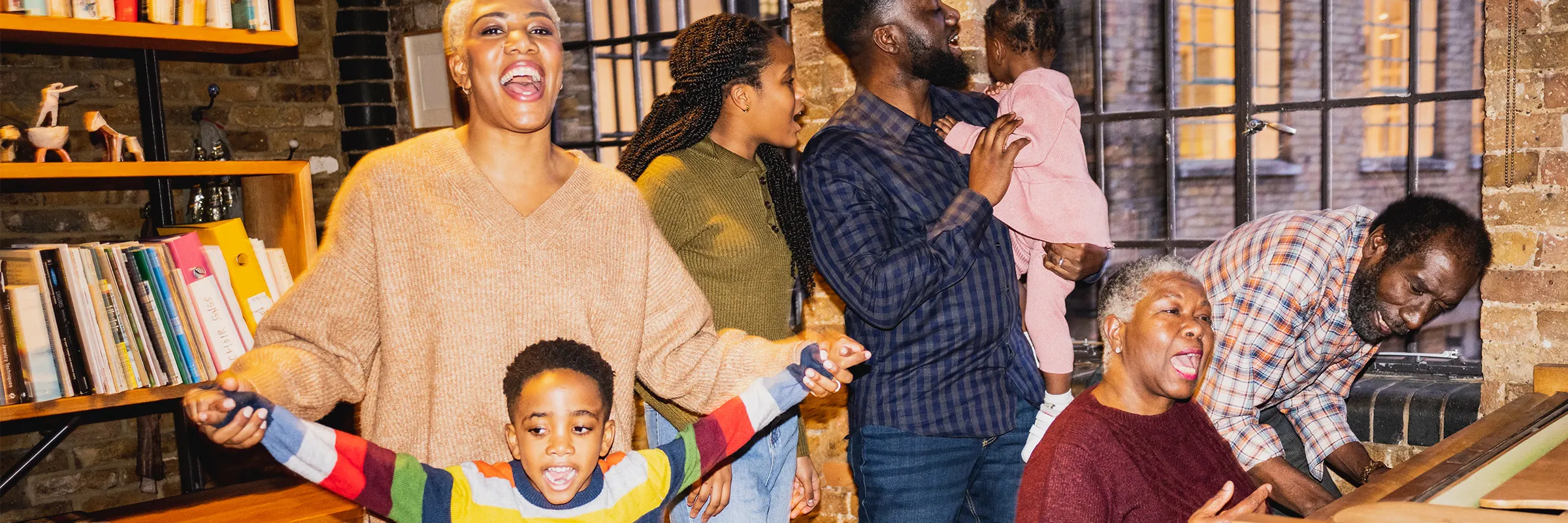Multi-generational family gathered around a piano and singing. 