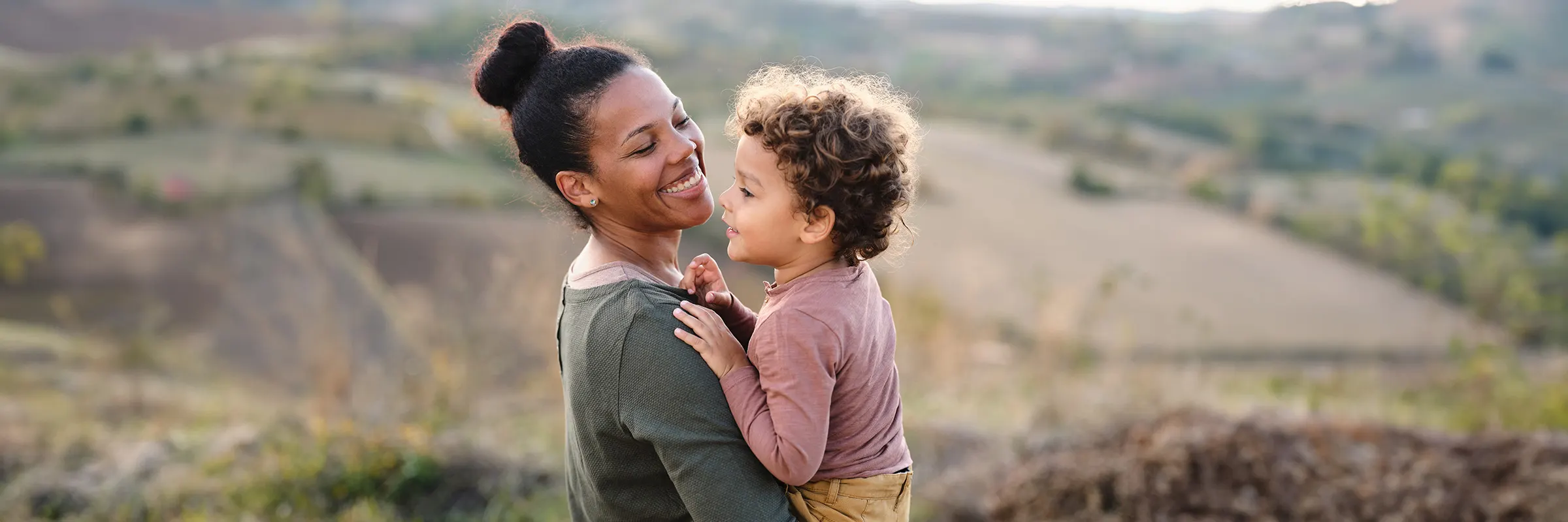 A smiling mother holds her child in her arms while outside.