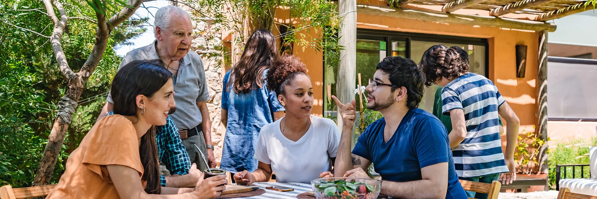 Friends and family sit around an outdoor dining table. 