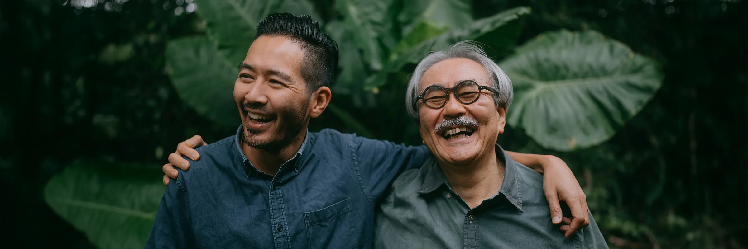 A young adult and older adult stand arm in arm outside laughing