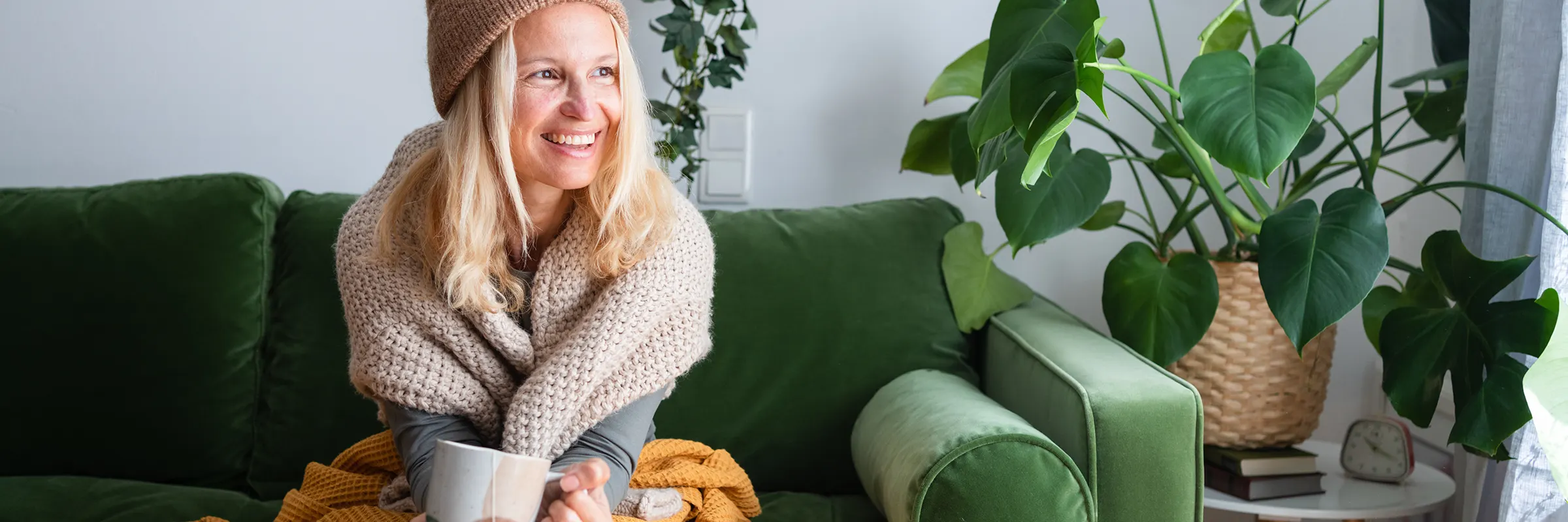 Person in warm clothes holding tea while sitting on sofa