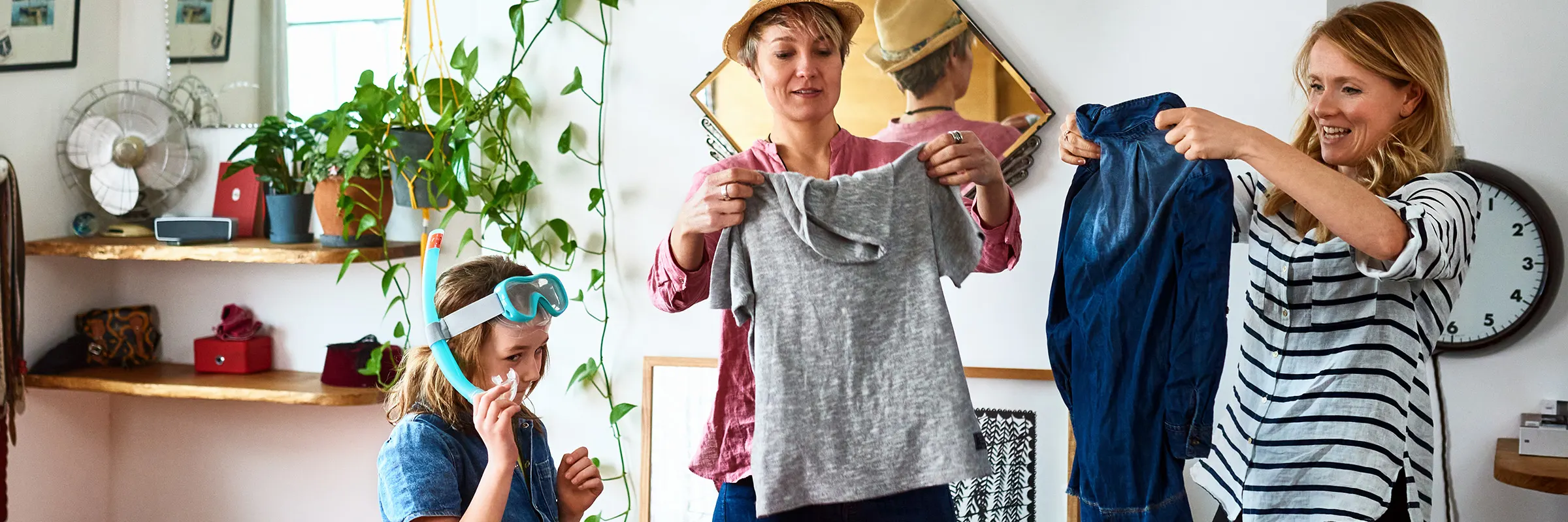 Couple packing their clothes for an upcoming trip while daughter wearing snorkeling gear helps