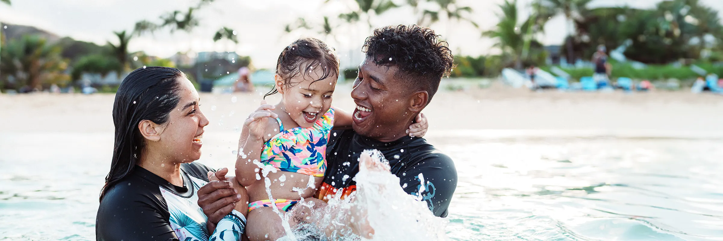 Young couple playing in the ocean water with their toddler. 