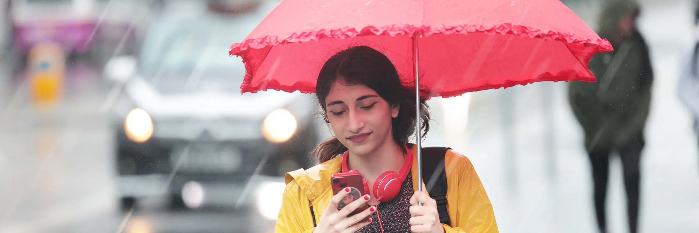 A woman walks along a city street in the rain with an umbrella and a phone.