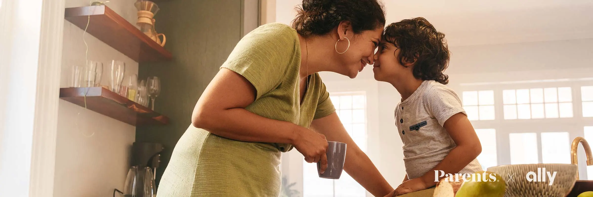 A mother and her young son sweetly touch noses as she stands in front of him sitting on the kitchen counter.