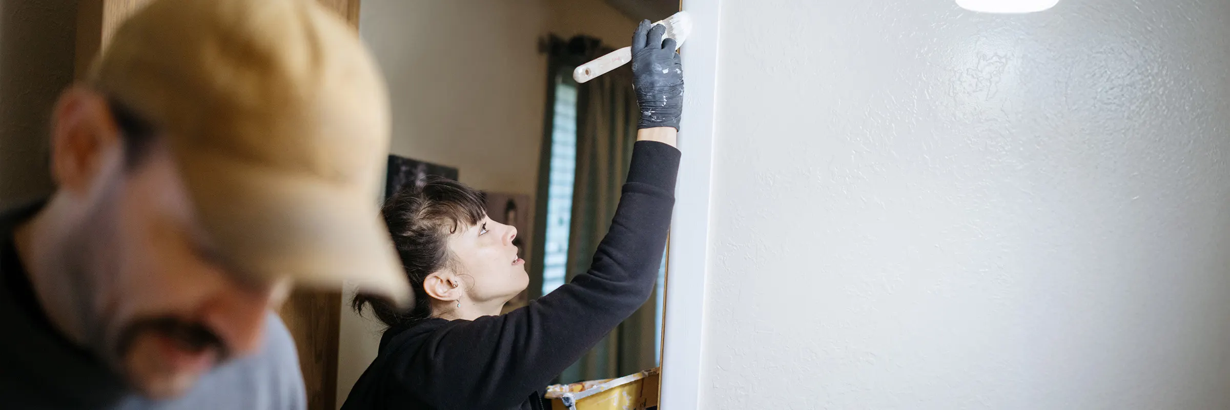 A couple is renovating their home. One person is painting the doorframe.  